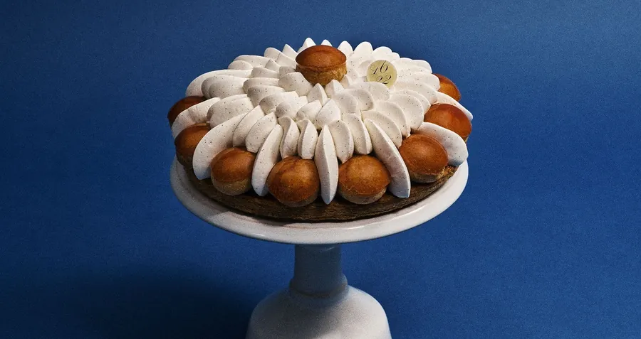 Saint-Honoré de Dalloyau con choux caramelizados y crema escudillada sobre un pie de tarta blanco ante un fondo azul intenso